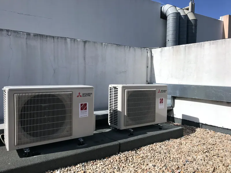 Duas unidades exteriores Mitsubishi Electric com etiqueta MDM, assentes em maciços de betão numa cobertura.