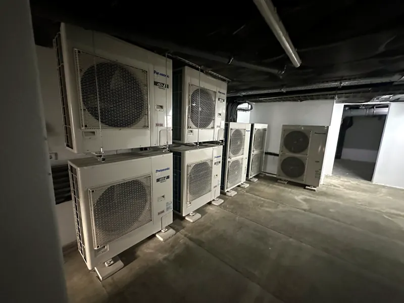 Sete unidades exteriores de um sistema VRF, alinhadas e sobrepostas numa central técnica em cave.