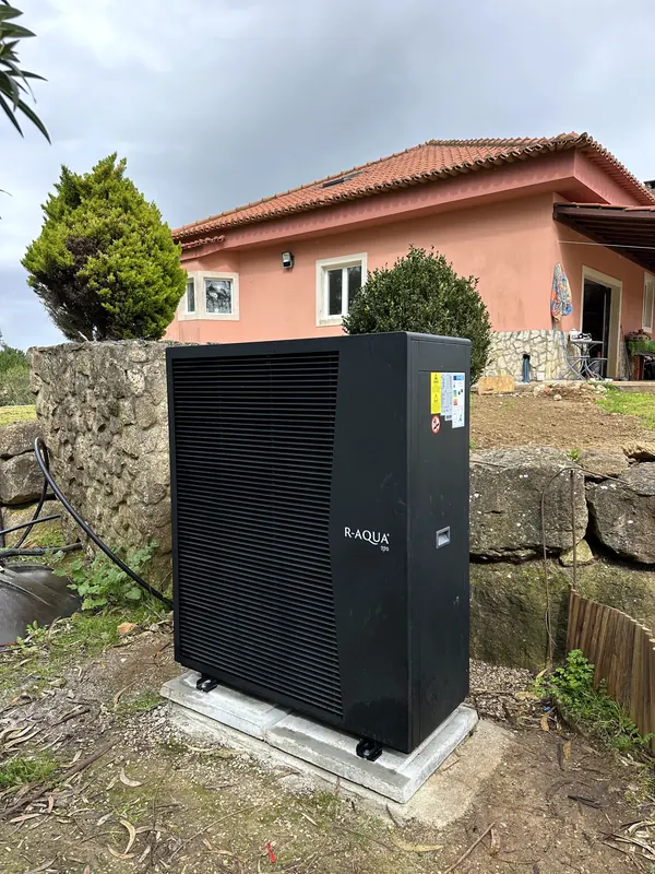 Bomba de calor monobloco preta assente em lajetas de betão, no jardim de uma moradia.