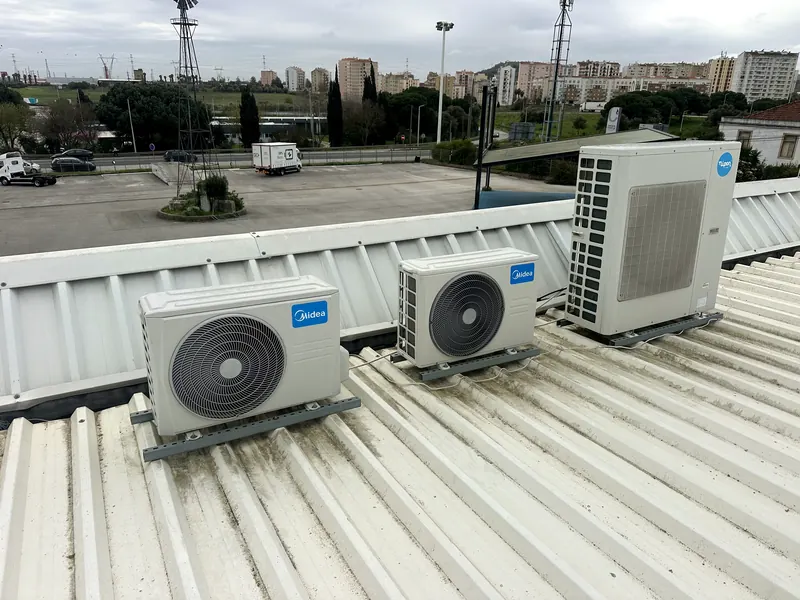 Três unidades exteriores Midea sobre perfis metálicos numa cobertura de chapa branca.