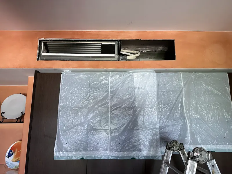Unidade de condutas embutida numa sanca sobre a cozinha, com o mobiliário protegido em plástico.