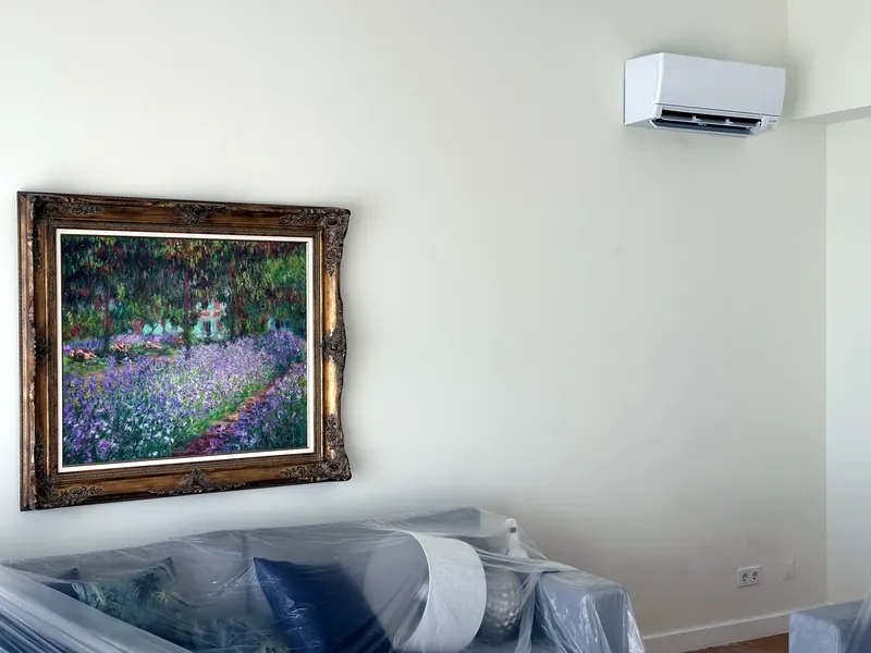 Unidade mural instalada numa sala, por cima de um quadro de moldura dourada, com o sofá coberto de plástico.