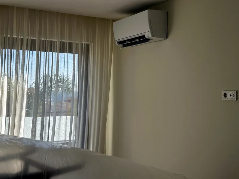 Unidade mural num quarto com cortinados translúcidos, junto ao teto, com a cama protegida.
