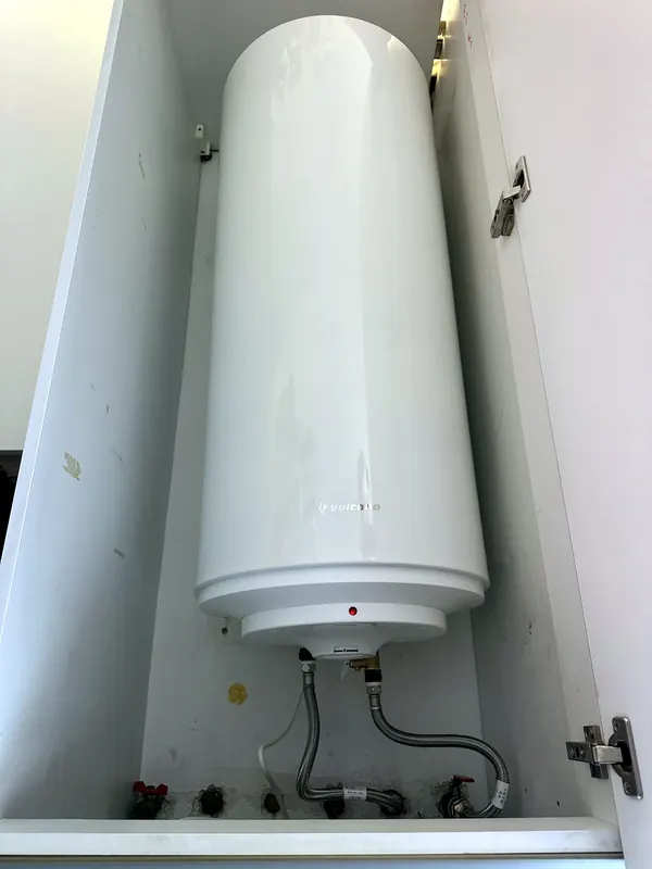 Termoacumulador instalado dentro de um armário, com ligações flexíveis.