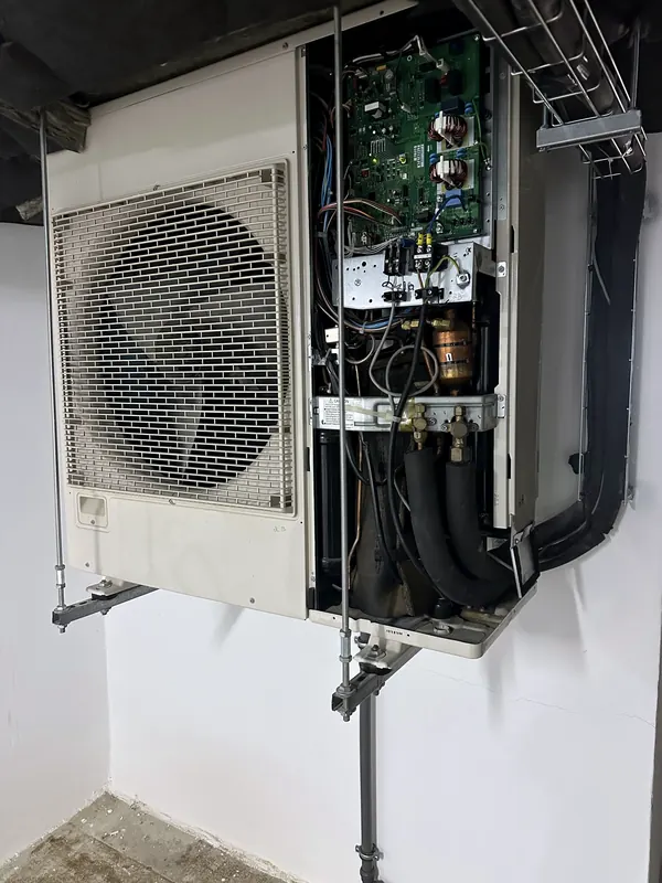 Unidade exterior suspensa por varão roscado, com o painel de comando aberto e a placa eletrónica à vista.