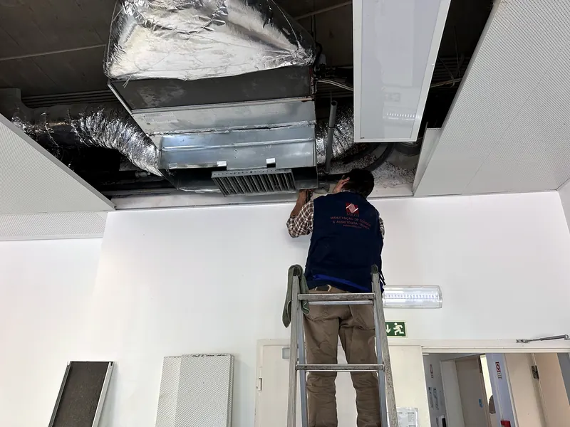 Técnico da MDM, de colete com o logótipo, num escadote a trabalhar numa conduta dentro do teto falso.