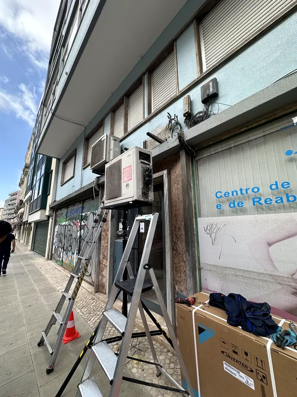 Escadotes e unidades antigas numa fachada comercial, com o equipamento novo ainda embalado no passeio.