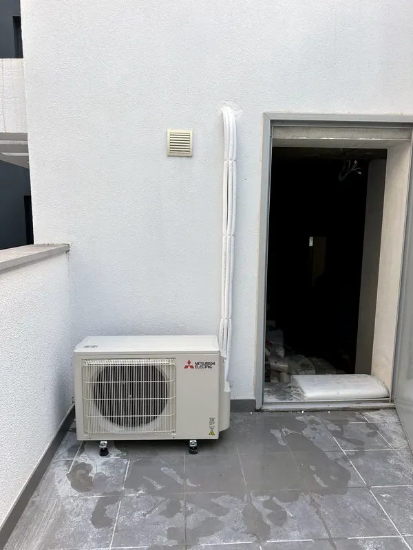 Unidade exterior Mitsubishi Electric num terraço, com a tubagem isolada a branco a descer a parede a prumo.