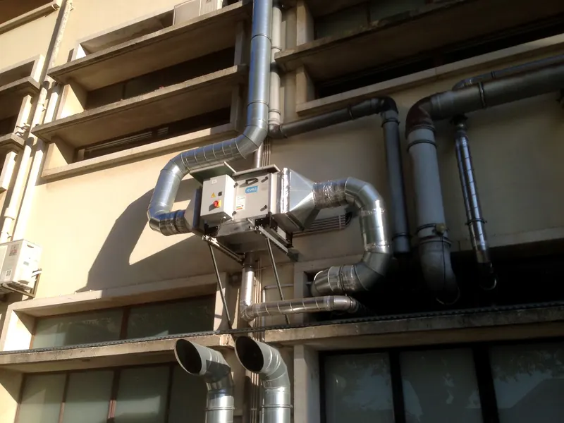 Condutas espiraladas em aço galvanizado e unidade de tratamento de ar montadas na fachada de um edifício.